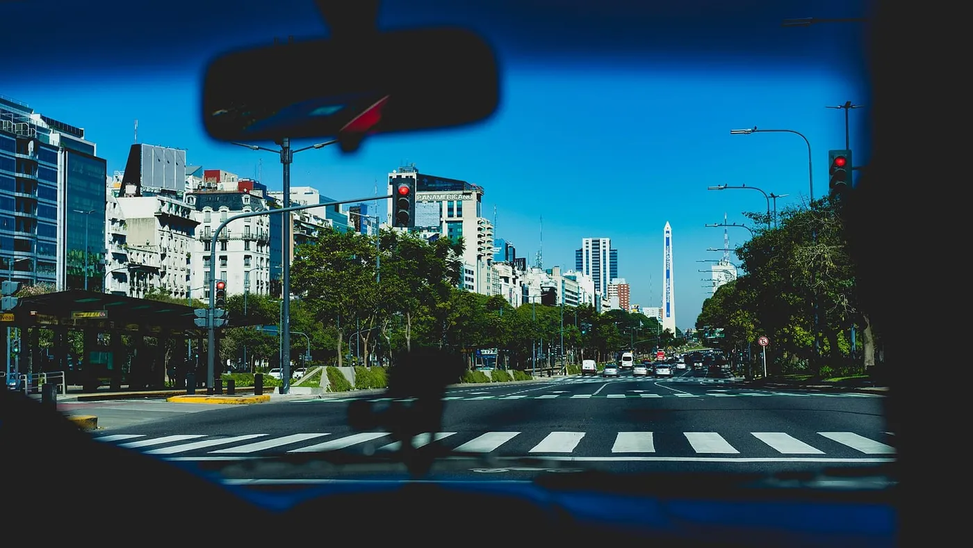 Vista desde el interior de un auto detenido en una avenida ancha de Buenos Aires, con edificios y árboles