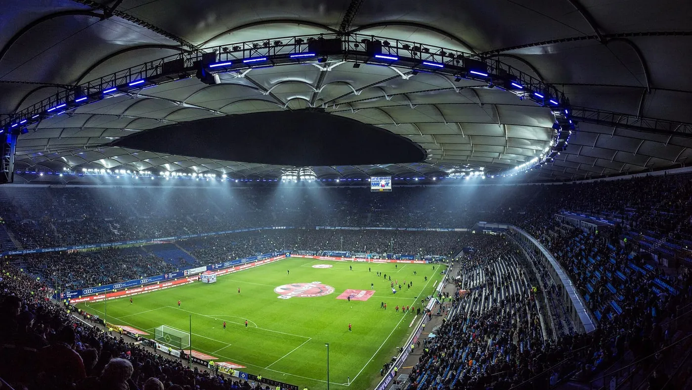 Un estadio de fútbol iluminado de noche, con las tribunas llenas de público