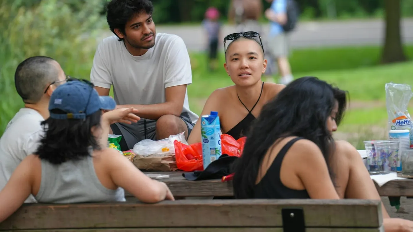 Un grupo de amigos conversa alrededor de una mesa de madera en un parque