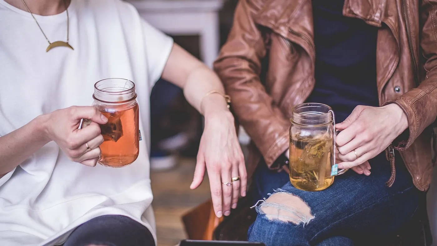 Dos personas sentadas una junto a la otra conversan con vasos de té en las manos