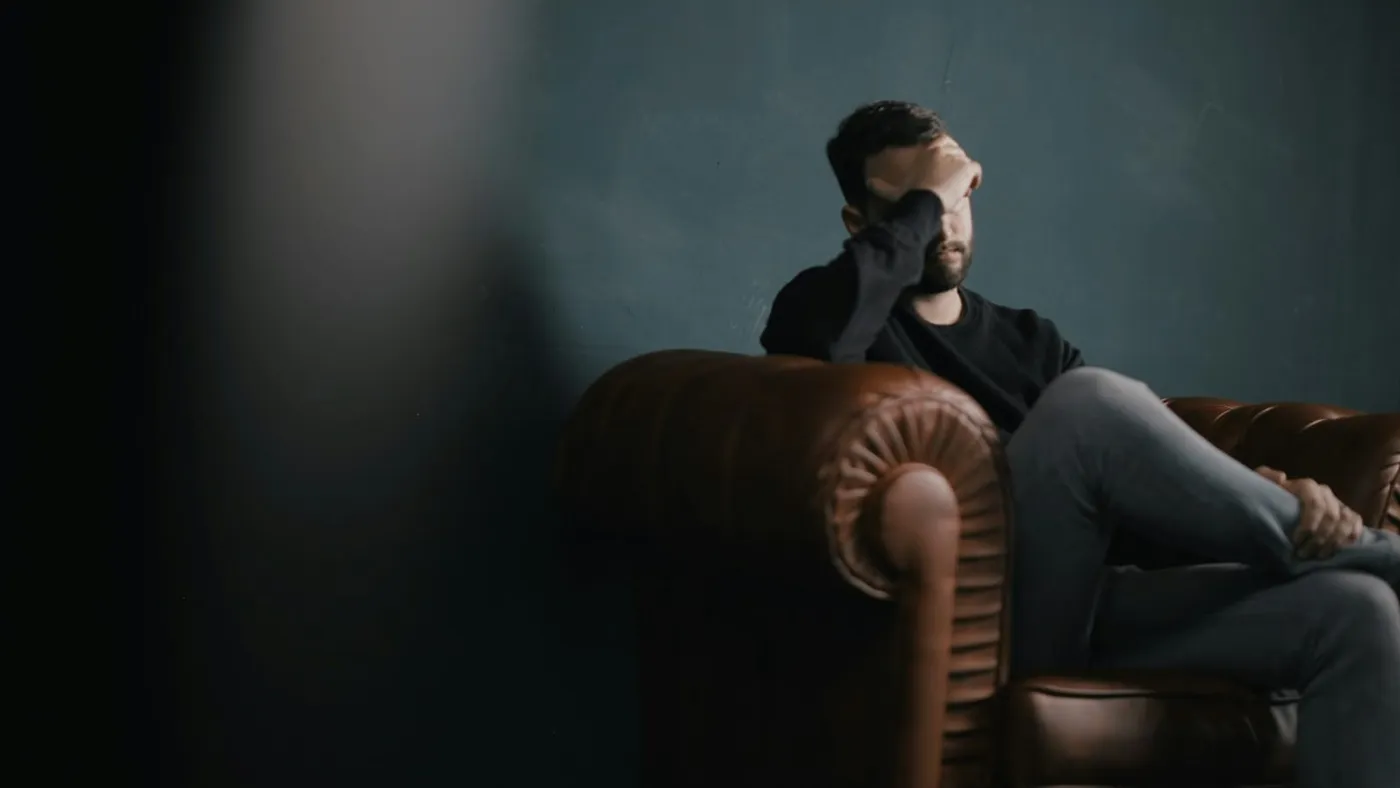 Un hombre sentado en un sillón se cubre la cara con las manos