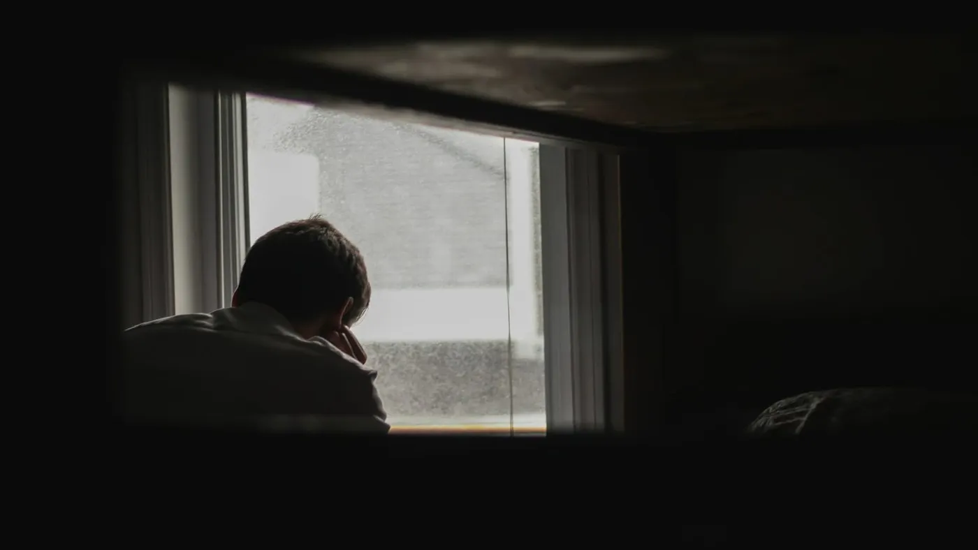 Un hombre mira por la ventana de una habitación en penumbra