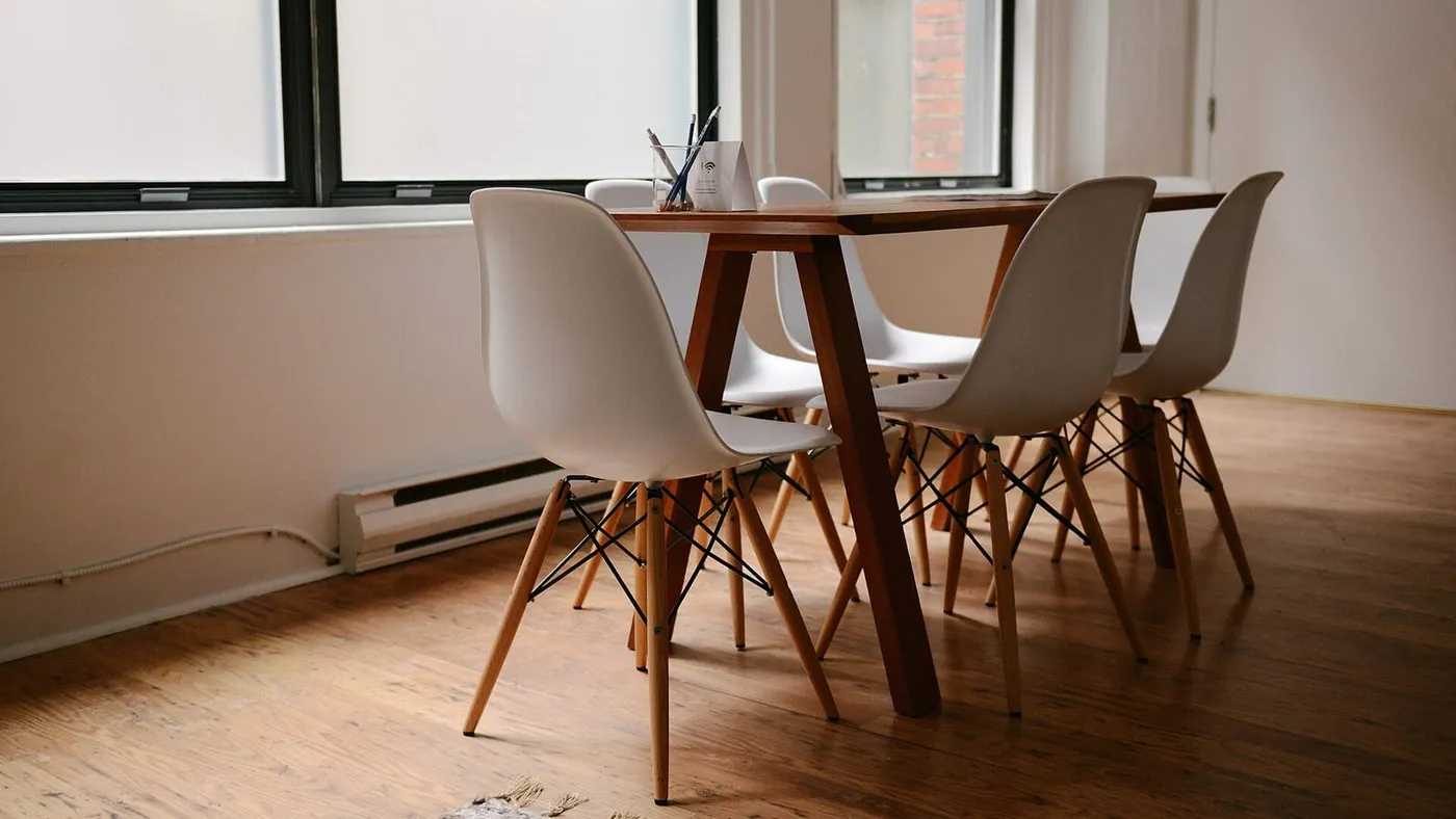 Una mesa de madera rodeada de sillas blancas en una sala de reuniones vacía e iluminada