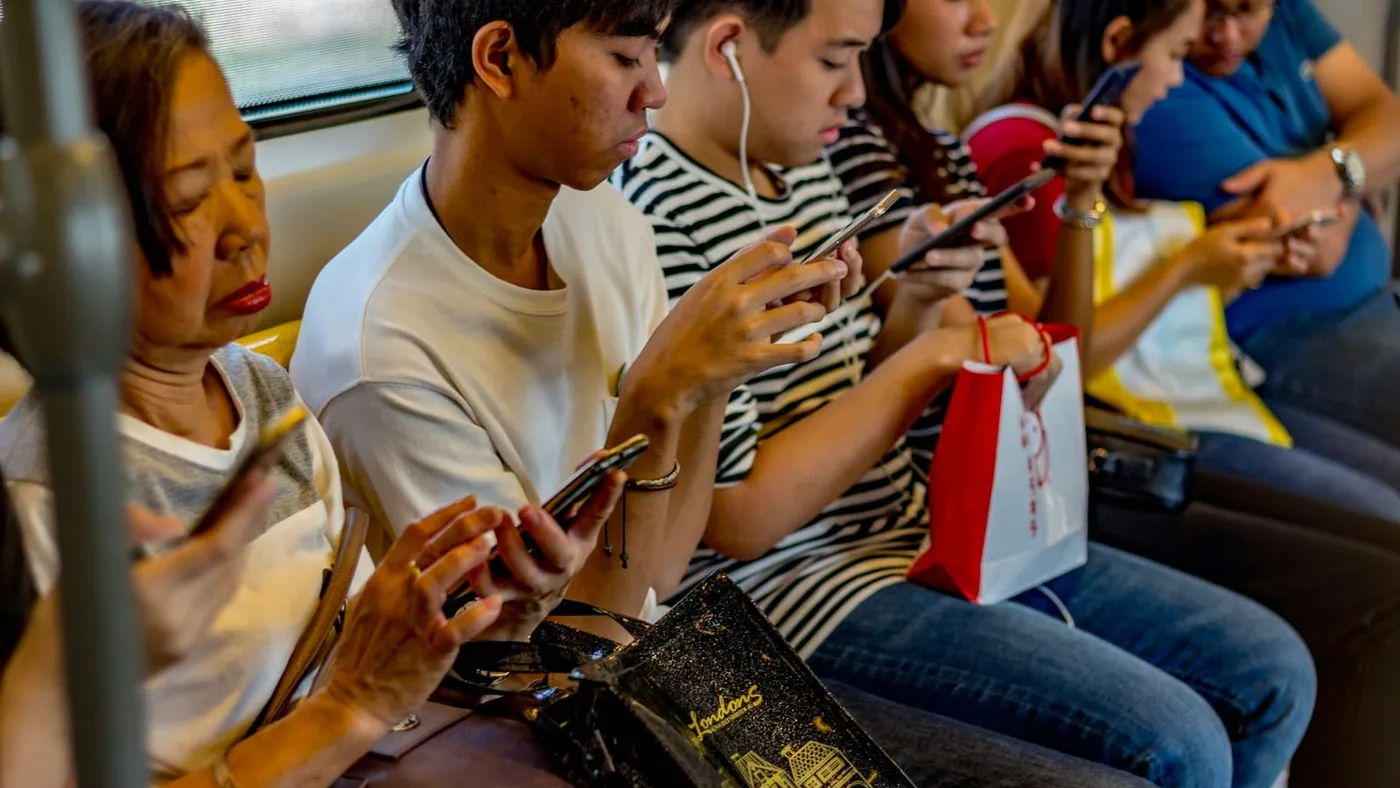 Varias personas jóvenes sentadas en un tren miran sus celulares