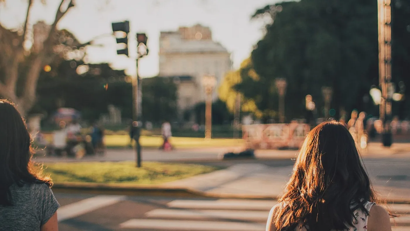 Dos mujeres esperan para cruzar una avenida arbolada de Buenos Aires al atardecer