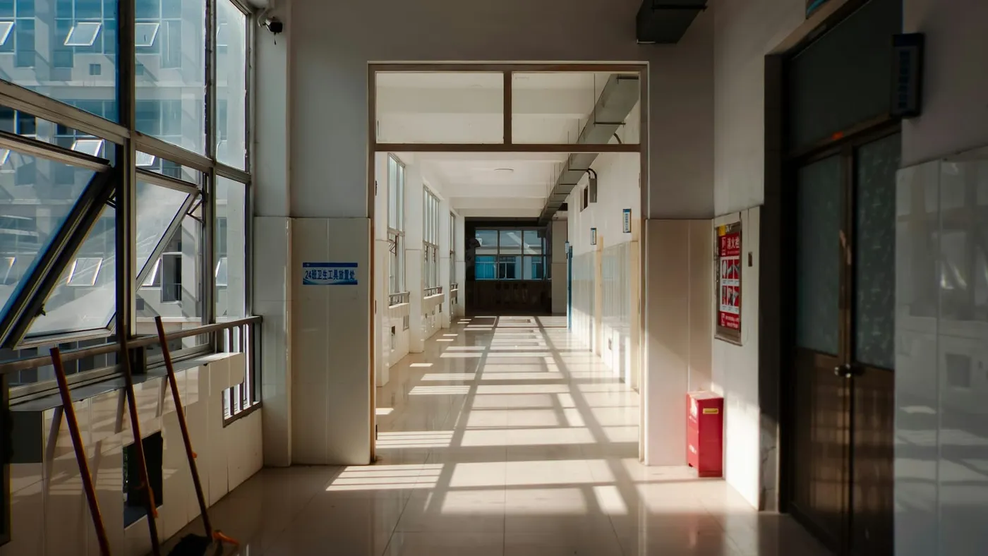 Un pasillo largo de escuela, vacío, con el sol entrando por los ventanales