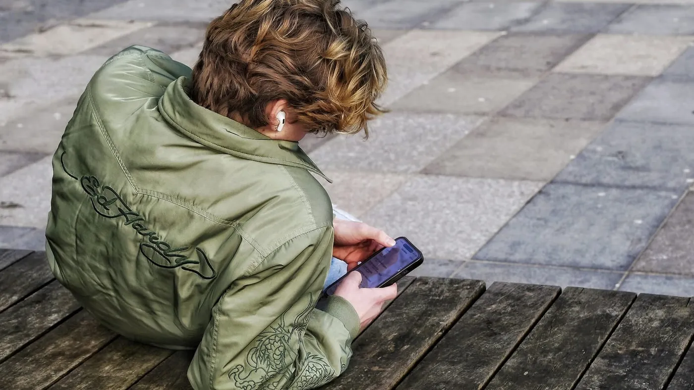 Un adolescente sentado en una plaza mira su celular