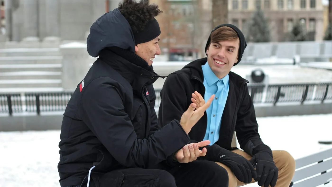 Dos jóvenes conversan sentados en un banco de una plaza, en un día de invierno