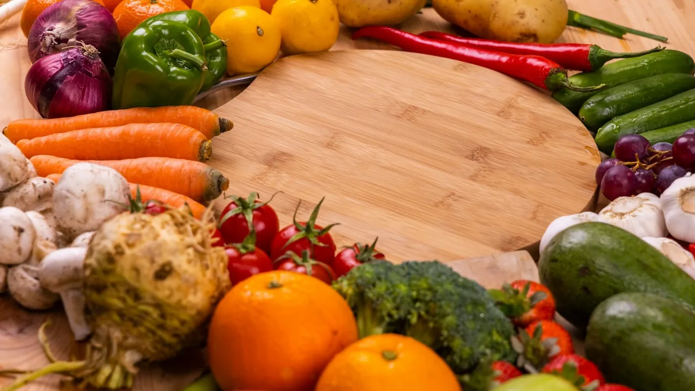 Verduras y frutas frescas alrededor de una tabla de madera sobre una mesa