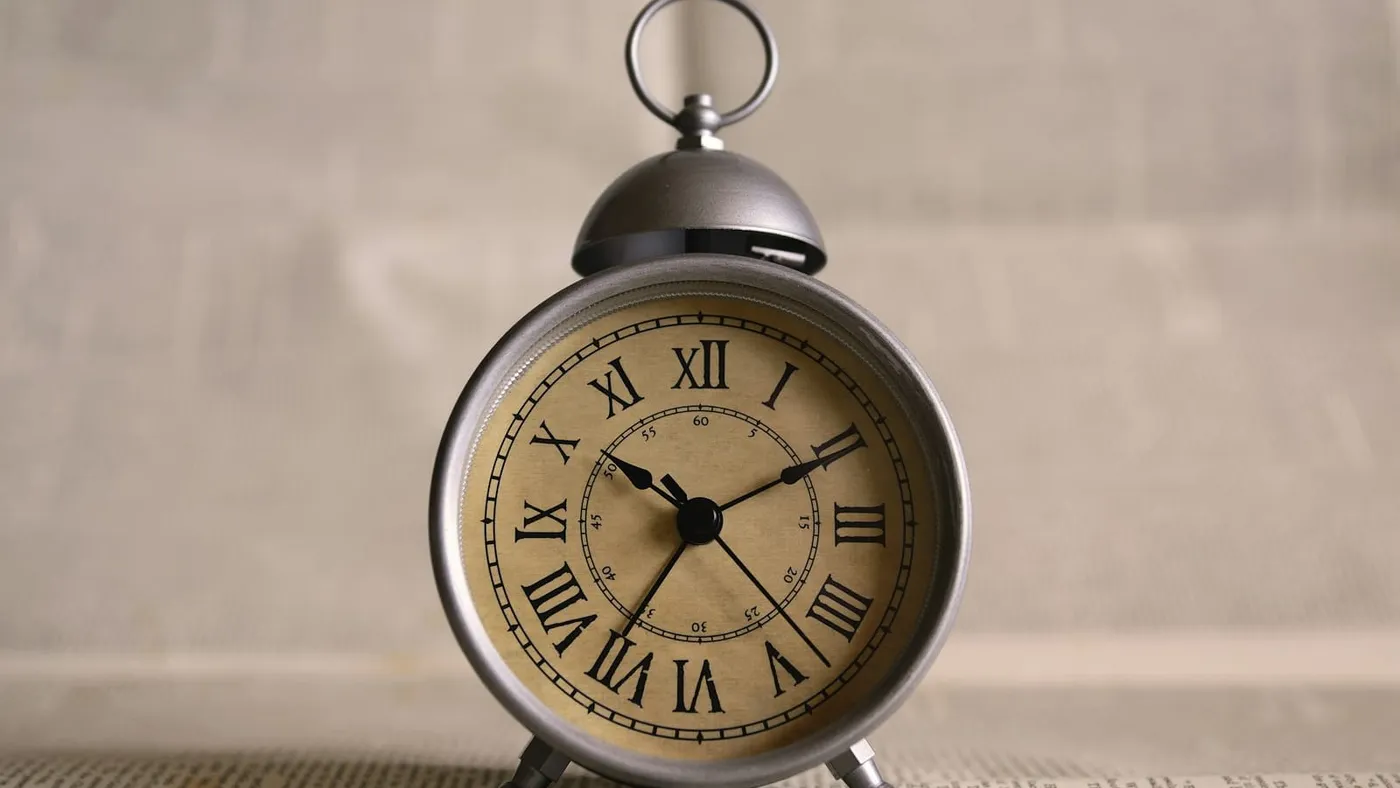 Un reloj despertador antiguo con números romanos apoyado sobre una mesa