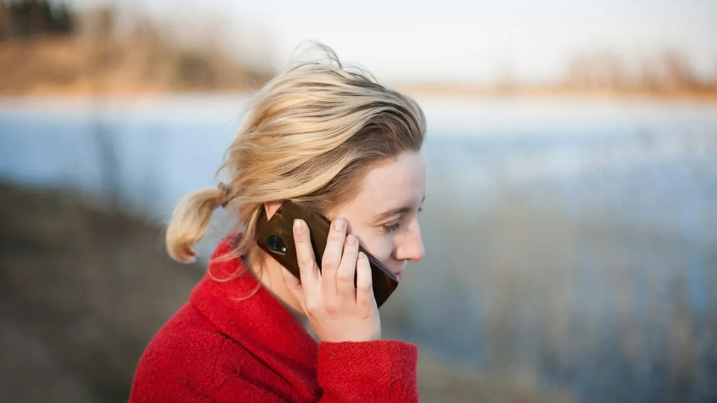 Una mujer de suéter rojo habla por celular al aire libre