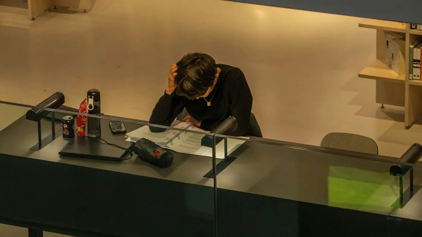 Una persona sentada detrás de un mostrador de oficina apoya la cabeza en una mano