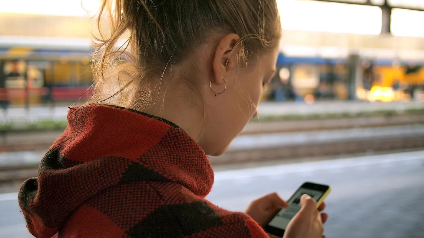 Una joven con bufanda mira su celular mientras espera en el andén de una estación de tren